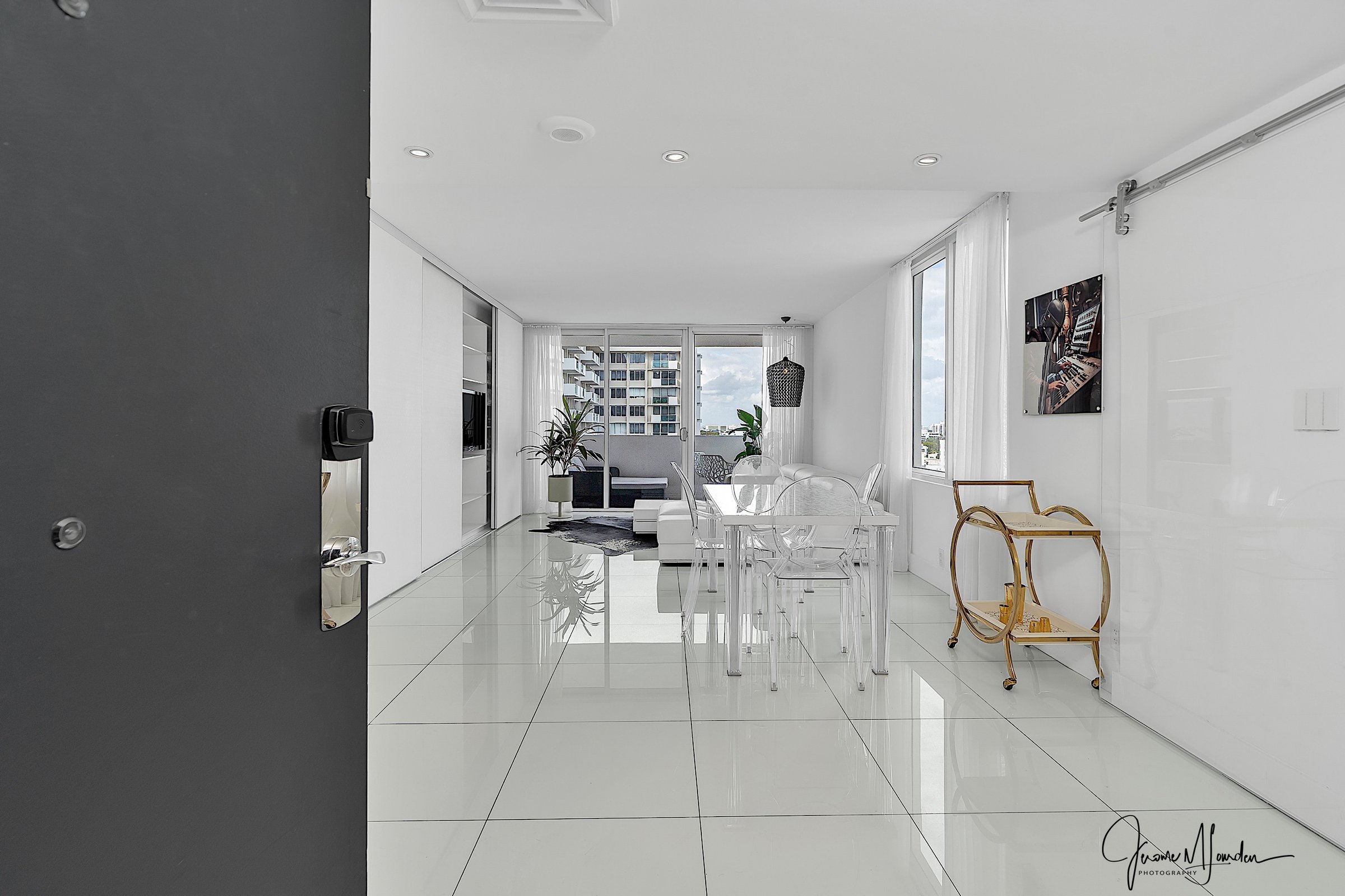 Entry view with ultra-white floors, ghost chairs, gold bar cart